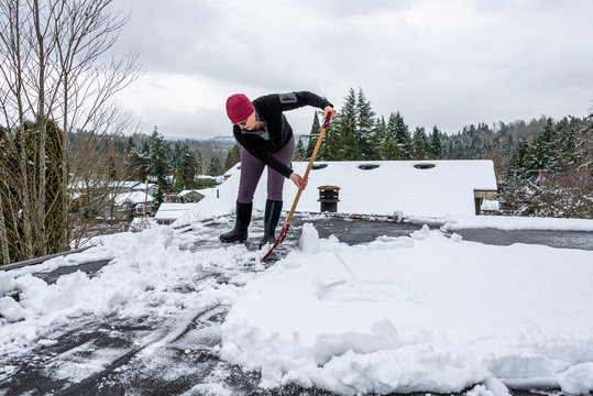 Mature Woman Shoveling Fresh Wet Snow Off A Flat Carport Roof