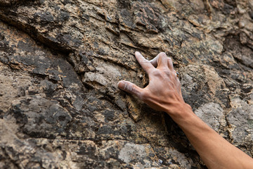 A close up view on the chalked hand of a traditional rock climber ascending a cliff. Reaching upwards searching for next grip on stone crag. Copy space on left