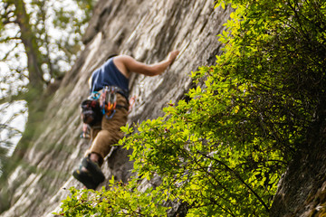 A low angle and selective focus view of a professional rock climber wearing gear belt and harness during an outdoor climb, with copy space to sides