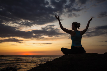 Fitness woman doing yoga exercises on the ocean coast at twilight.
