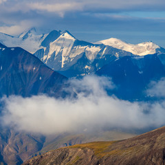 Mountain landscape, morning light. Snow-capped peaks rise above the clouds.