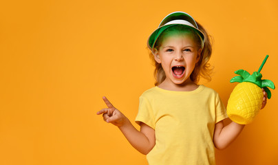 Little smiling girl in yellow t-shirt and hat holding fresh fruit juice in pineapple shaped bottle with straw and feeling fun