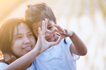 Asian mother and daughter making heart shape with hands together with love in the field with sunlight