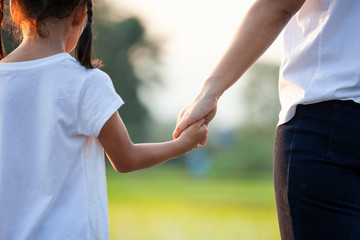 Asian child girl holding her mother hands together with love in the field with sunlight