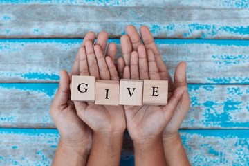 Alphabet letter wooden blocks with words GIVE in child and parents hands. Family and charity concept