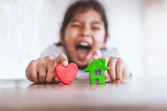 Cute asian child girl playing with plasticine clay house and heart with fun. Happy family and warm house concept.