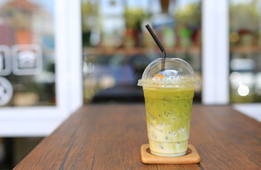 Iced matcha green tea latte with milk with brown straw in take away cup on wooden table at cafe.