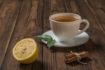 Obraz na płótnie Canvas A Cup of fresh tea with half a lemon and cinnamon sticks on a wooden table.