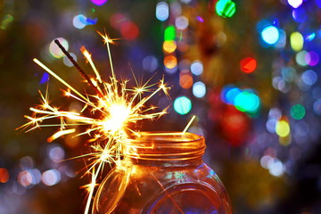 Sparks from burning Sparkler candle in glass jar on wooden table on blurred background with glowing...
