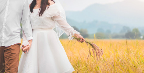 Bride and groom lovely couple hold of hands at meadow outdoor location. Bride holding flower grass in her hand , copy space.