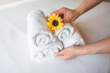 Cropped shot view of hotel maid putting flower and arranging the set of towels on bed. Conceptual of female chambermaid making bed in hotel room.