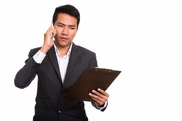 Young Asian businessman reading on clipboard while talking on mo