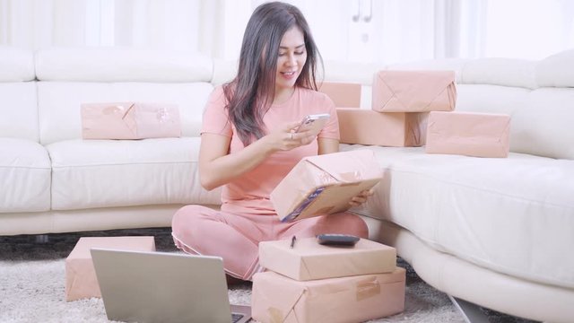 Beautiful online seller taking picture of customer address on the package in the living room at home. Small Medium Enterprise or Startup concept. Shot in 4k resolution