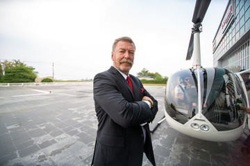 confident businessman standing in front of private helicopter 