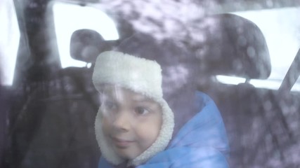 little boy rides in the car in the back seat in winter forest and looks out the window