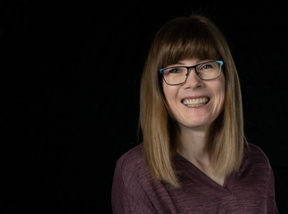 Middle aged woman with glasses laughing, isolated on dark background