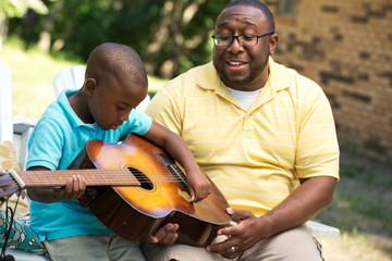 Father teaaching his his son to play the guitar.
