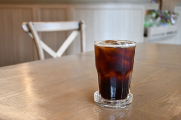 A glass of ice Americano on wooden table in cafe.