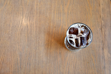 A glass of ice Americano on wooden table in cafe.