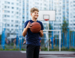 Cute boy in blue t shirt plays basketball on city playground. Active teen enjoying outdoor game with orange ball. Hobby, active lifestyle, sport for kids.	