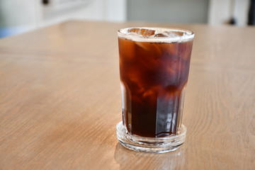 A glass of ice Americano on wooden table in cafe.