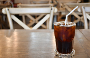 A glass of ice Americano on wooden table in cafe.