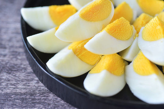 Slice boild eggs with unopened egg in  black wooden plate