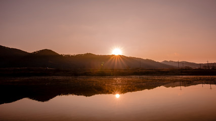 The sun rising over the mountains and the sun reflected in the river.