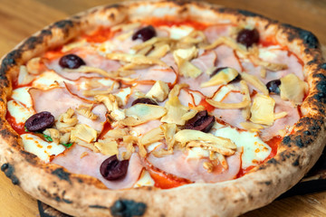 Freshly baked pizza with cheese, sauce, vegetables and ham on a wooden table