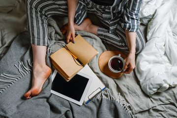 Faceless portait of woman sitting in her bed with tablet and tea, selective focus