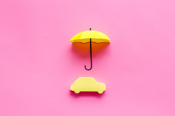 Car insurance. Automobile toy under umbrella on pink background top-down copy space