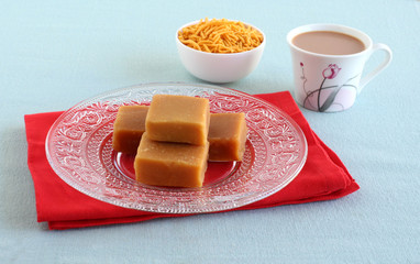 Mysore pak, a traditional, popular, and delicious sweet dish native to the city of Mysore, Karnataka, India, on a glass plate with tea and bhujia, which is a snack.
