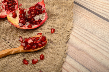 Chunks of juicy ripe pomegranate and pomegranate seeds on a wooden spoon on a background of rough homespun fabric. Close up.