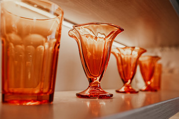 identical stylish textured glasses and vases of bright orange glass for drinks stand on wooden shelves in the interior of the room