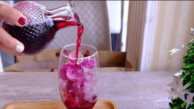 women hand pour red fruit water drink in to wine glass on circle ice mix petal plower