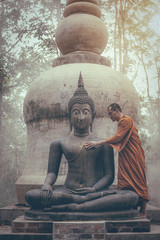 Monk scrubbing buddha statue at temple in Thailand