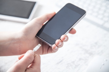 Business girl charging smartphone in office.