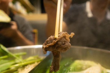 Close up of chopsticks picking up pork from hotpot.