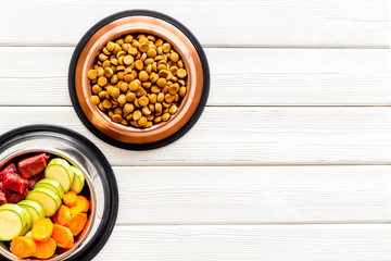 Healthy feed for cats and dogs. Bowls full of dry feed, meat and vegetables on white wooden background top-down copy space