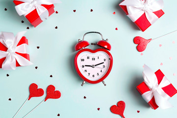 Valentine's day composition with alarm clock, gift boxes and hearts on a blue background. F
