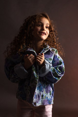 Studio portrait of a little girl with long curly hair, in a colorful jacket and light shorts.