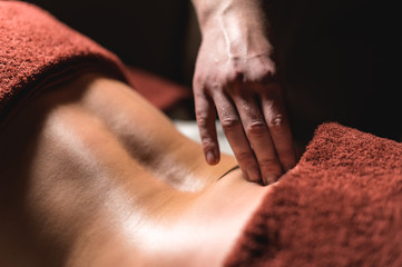 Close-up male hand of a professional physiotherapist masseur doing lumbar massage to a female patient in a massage luxury room with dim light