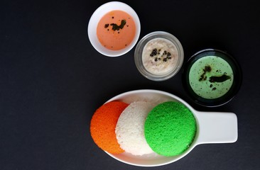 Obraz na płótnie Canvas Tiranga Idli or Tricolor Idly cooked in Indian National Flag colors - saffron or orange, white and green. Served with tiranga chutney. Concept for Indian Independence or Republic day greeting card. 