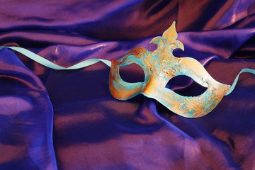 Photo of elegant and delicate blue and bronze Venetian mask over purple silk background