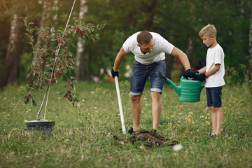 Family on a yard. Father with son planting a tree. Boy with a green funnel