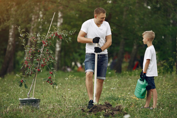 Family on a yard. Father with son planting a tree. Boy with a green funnel