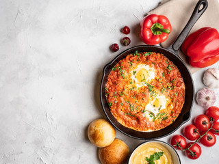 Shakshuka with bell pepper, tomatoes, hummus and rolls. Top view, place for text.