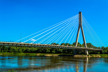 Modern bridge in Warsaw. Sunny summer day with a blue sky and green trees. Horizontal photo.