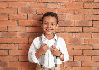 Cute fashionable African-American boy near brick wall