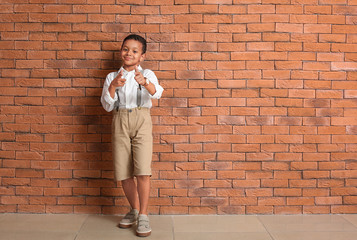 Cute fashionable African-American boy pointing at viewer near brick wall